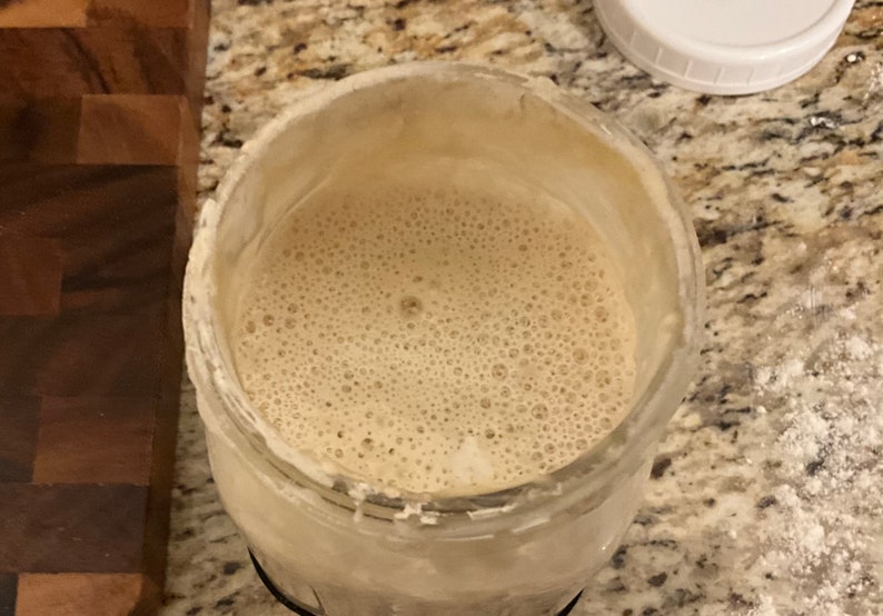 May include: A glass jar filled with a light brown liquid with a foamy texture. The liquid is bubbling and has a light brown color.
