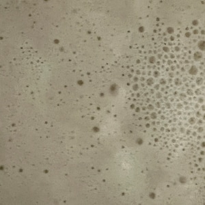 May include: Close-up of a light brown surface with a pattern of small, round bubbles.