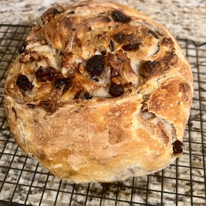 May include: A freshly baked loaf of bread with raisins and walnuts. The bread has a golden brown crust and is slightly cracked on the surface.