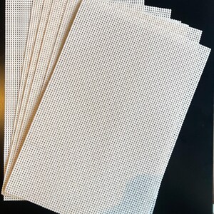 Puede incluir: Una pila de hojas rectangulares de malla plástica de color blanco hueso, con una cuadrícula uniforme de pequeños orificios espaciados equitativamente. Las hojas están dispuestas en abanico, mostrando la textura rígida y perforada.