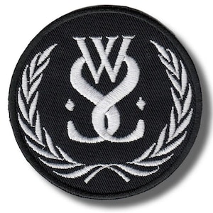May include: A circular black embroidered patch featuring a white stitched design of the letters W and S intertwined in the center. The emblem is framed by a white laurel wreath pattern and includes two small white diamond shapes on the sides.