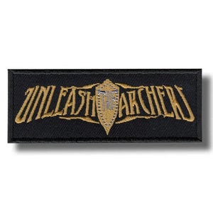 May include: A rectangular black embroidered patch featuring the gold-colored text UNLEASH THE ARCHERS. In the center, a gold shield-shaped emblem is displayed with silver detailing, positioned between the words UNLEASH and THE ARCHERS.