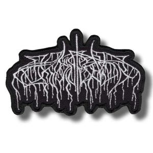 May include: A black embroidered patch featuring white thread in a stylised, illegible, jagged, and dripping font design. The patch has a thick black border and an irregular, organic shape that follows the contours of the intricate white lettering.