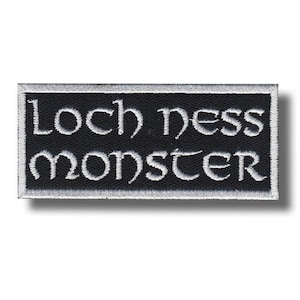 Może przedstawiać: Prostokątna haftowana naszywka z czarnym tłem i białą obwódką. Napis "Loch Ness Monster" jest wyhaftowany białą nicią na środku stylizowaną czcionką szeryfową, ułożony w dwóch liniach z wyrazami umieszczonymi jeden pod drugim.