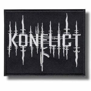 Puede incluir: Un parche rectangular bordado en negro con el texto blanco KONFLICT en una fuente estilizada. Las letras están integradas con líneas verticales blancas que se asemejan a alambre de espino o cuchillas afiladas, creando un diseño.