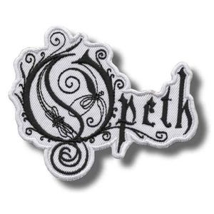 May include: A white embroidered patch featuring the black Opeth logo. The design includes a large, stylized letter O with intricate, swirling filigree patterns integrated into the typography, followed by the lowercase letters peth in a gothic font.