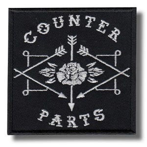Può includere: Una toppa quadrata ricamata nera con cuciture bianche. Il testo COUNTER PARTS è arcuato sopra e sotto un disegno centrale a rosa. Due frecce incrociate formano una forma a diamante attorno alla rosa, con ulteriori dettagli di frecce esterne.