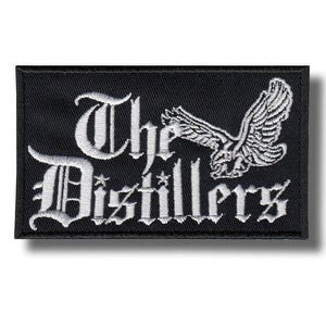 Puede incluir: Un parche rectangular bordado en negro que presenta el texto blanco The Distillers en una fuente gótica. A la derecha del texto hay un gráfico bordado en blanco detallado de un águila con las alas extendidas en posición de vuelo.