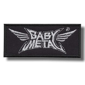 Può includere: Una toppa rettangolare ricamata nera con il testo bianco BABY METAL in un carattere stilizzato con accenti a forma di ala sui lati. Il disegno è cucito con filo bianco su una base di tessuto nero con un bordo nero circostante.