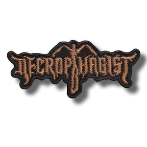 以下が含まれることがあります： 黒い刺繍ワッペン。銅色のギザギザとした独特なフォントで「Necrophagist」という文字が描かれている。文字の中央には両手を広げた人物のシルエットが組み込まれており、全体が太い黒の縁取りで囲まれている。