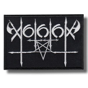 Op de afbeelding: Een rechthoekige zwarte geborduurde patch met wit stiksel. Het ontwerp toont een gestileerd, symmetrisch logo met scherpe, puntige verticale lijnen, halvemaanvormen en een centraal vijfpuntig ster-pentagramsymbool.