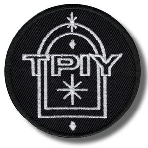 Könnte beinhalten: Ein kreisförmiger, schwarz bestickter Aufnäher mit einem weißen, gestickten Torbogen-Design. Innerhalb des Bogens sind die Buchstaben TPIY in Weiß gestickt, ergänzt durch ein kleines Sternsymbol darüber und einen großen achtstrahligen Stern darunter.