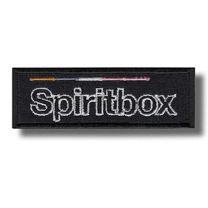 Op de afbeelding: Een rechthoekige zwarte geborduurde patch met het woord Spiritbox in witte hoofdletters. Boven de tekst staat een dunne horizontale lijn met een kleurverloop van oranje naar grijs, wit en uiteindelijk naar een zachte roze kleur.