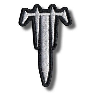 Puede incluir: Un parche bordado con un diseño estilizado en plata y negro con forma de espada o daga vertical con una cruceta. El emblema tiene un borde grueso cosido en negro y un relleno de hilo plateado metálico, creando una silueta afilada.