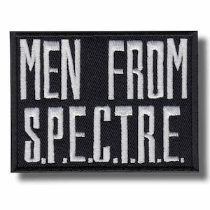 May include: A rectangular black embroidered patch featuring the white text MEN FROM S.P.E.C.T.R.E. arranged in two lines. The lettering is in a bold, sans-serif font with a visible stitched texture throughout the entire surface of the patch.