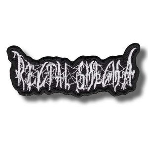 Può includere: Una toppa ricamata nera con dettagli in filo bianco. Il design presenta lettere stilizzate e frastagliate che formano la scritta Rectal Smegma, con intricate cuciture bianche a ragnatela che collegano i caratteri sullo sfondo in tessuto nero.