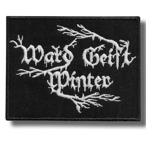 Könnte beinhalten: Ein rechteckiger, schwarz bestickter Aufnäher mit weißem Text, der Wald Geist Winter lautet. Die Schriftzeichen sind mit astartigen Verzierungen gestaltet, die die Wörter einrahmen und einen starken Kontrast zum dunklen Stoff bilden.