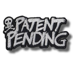 Puede incluir: Un parche bordado en blanco y negro que presenta el texto "PATENT PENDING" en una fuente audaz y estilizada. A la izquierda del texto hay un pequeño icono blanco de una calavera con tibias cruzadas. El parche tiene un fondo negro con costuras.
