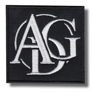 May include: A square black embroidered patch featuring the white stitched letters AG in a serif font. The letters are intertwined with a circular border element, creating a bold monogram design with a clean, textured finish on a fabric base.