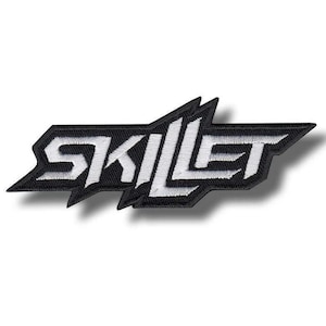 May include: A black and white embroidered patch featuring the word SKILLET in a stylized, angular, and sharp-edged font. The design consists of white lettering with a thick black border, creating a bold, high-contrast graphic emblem.
