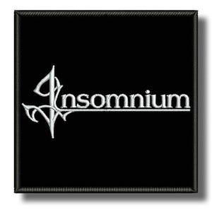Pode incluir: Um emblema quadrado bordado em preto com o texto branco Insomnium em uma fonte estilizada. A letra I é alongada com pontas decorativas afiadas que se estendem da base e das laterais, criando um design de logotipo distinto em fundo escuro.