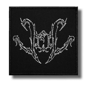 May include: A square black patch featuring a white embroidered design in the center. The embroidery consists of intricate, sharp, and symmetrical lines that form a stylized, abstract emblem with pointed edges and decorative flourishes.