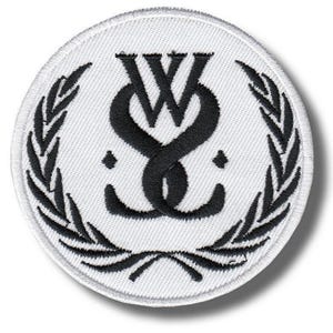 May include: A circular embroidered patch featuring a white background with a black stitched border. The center displays a stylized black monogram of the letters W and S intertwined, flanked by two small black diamonds and a black laurel wreath design.
