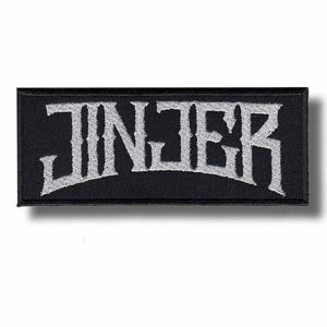 May include: A rectangular black embroidered patch featuring the word JINJER in a stylized, jagged white font. The lettering is centered on the fabric, which has a visible stitched texture and a clean, straight border around the entire perimeter.