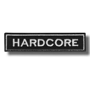 Könnte beinhalten: Ein rechteckiger gestickter Aufnäher mit schwarzem Hintergrund und weißem Rand. Das Wort HARDCORE ist in weißen Großbuchstaben in der Mitte des Aufnähers eingestickt. Das Design zeigt eine klare, fette Schrift und eine gestickte Stoffstruktur.