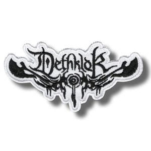 May include: A white embroidered patch featuring the black text Dethklok in a stylised gothic font. The design includes symmetrical black wing-like shapes extending from the sides and a central circular emblem with downward-pointing accents.