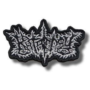 May include: An embroidered patch featuring a black background with white thread forming a dense, jagged, and illegible text design. The patch has a thick black border that follows the irregular, spiky outline of the central graphic element.