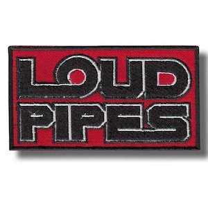 Puede incluir: Un parche rectangular bordado que presenta un fondo rojo vibrante con un borde negro. El texto LOUD PIPES está cosido en letras negras en negrita con un fino contorno blanco, centrado en dos líneas sobre la superficie de la tela.