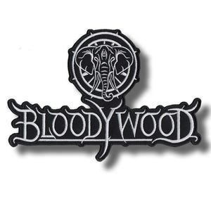 Può includere: Una toppa ricamata in bianco e nero caratterizzata da un emblema circolare con una testa di elefante stilizzata nella parte superiore, collegata a uno stendardo orizzontale sottostante che mostra il testo BLOODYWOOD in un carattere bianco audace.