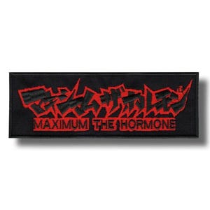 May include: A rectangular black embroidered patch featuring red Japanese kanji characters at the top and the text MAXIMUM THE HORMONE in red capital letters underneath. The design has a jagged, sharp-edged aesthetic with a black border.