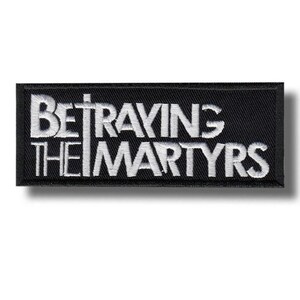 May include: A rectangular black embroidered patch featuring the white text BETRAYING THE MARTYRS in a bold, stylised font. The design is oriented horizontally with a clean, stitched border surrounding the lettering on a dark fabric background.