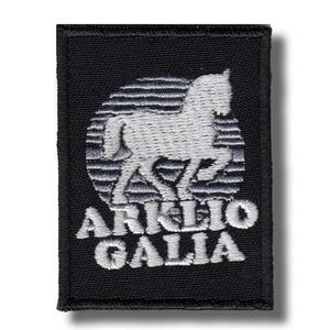 Op de afbeelding: Een rechthoekige zwarte geborduurde patch met het silhouet van een wit paard gecentreerd over een cirkelvormige achtergrond van horizontale lijnen. De tekst "ARKLIO GALIA" is in witte hoofdletters onder de paardenafbeelding geborduurd.