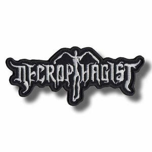 May include: A black embroidered patch featuring the white text Necrophagist in a stylised, jagged font. The design includes a central white silhouette of a figure with outstretched arms integrated into the lettering, all on a black background.