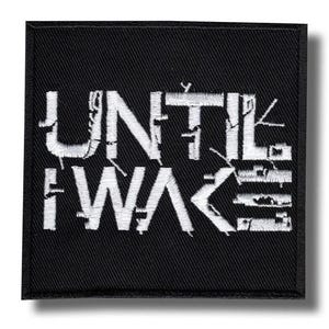 May include: A square black embroidered patch featuring the white text UNTIL I WAKE in a stylized, fragmented font. The letters have a distressed, glitch-like appearance with horizontal lines and broken segments throughout the white stitching.