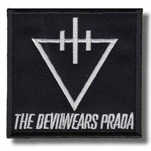 Puede incluir: Un parche cuadrado bordado en negro que presenta un símbolo de triángulo invertido blanco con un diseño en forma de cruz vertical encima. El texto THE DEVILWEARS PRADA está bordado en letras mayúsculas blancas a lo largo del borde inferior.