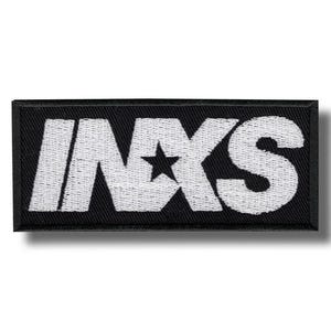 Op de afbeelding: Een rechthoekige geborduurde patch met een zwarte achtergrond en wit stiksel. De tekst INXS is weergegeven in een vet, schreefloos lettertype, waarbij een vijfpuntige ster de letter X vervangt. Het ontwerp heeft een zwarte geborduurde rand.