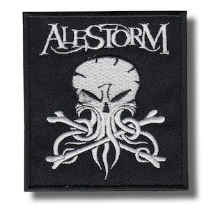 Puede incluir: Un parche rectangular bordado en negro con el texto blanco ALESTORM en la parte superior. Debajo del texto hay un gráfico bordado en blanco de una calavera con rasgos similares a tentáculos y huesos cruzados, creando un diseño de alto contraste.