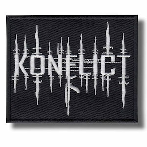 May include: A rectangular black embroidered patch featuring the white text KONFLICT. The letters are stylized with vertical white lines resembling barbed wire or sharp spikes that extend above and below the text, creating a jagged, distressed appearance across the center of the patch.
