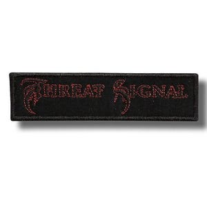 Op de afbeelding: Een rechthoekige zwarte geborduurde patch met de tekst THREAT SIGNAL in een gestileerd rood lettertype. De letters hebben een scherp, hoekig ontwerp met decoratieve krullen aan de eerste en laatste letter, op een effen zwarte achtergrond.