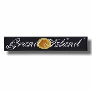 May include: A rectangular black embroidered patch featuring the white cursive text Grand Island. The word Grand is on the left and Island is on the right, separated by a circular yellow and orange sun-like emblem in the centre of the patch.