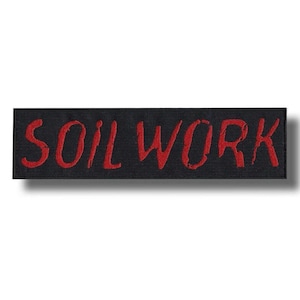 Könnte beinhalten: Ein rechteckiger, schwarz bestickter Aufnäher mit dem Wort SOILWORK in einer abgenutzten, gezackten roten Schriftart. Die Buchstaben sind direkt auf den schwarzen Stoffgrund gestickt, was einen starken Kontrast zwischen dem dunklen Hintergrund und dem roten Text erzeugt.