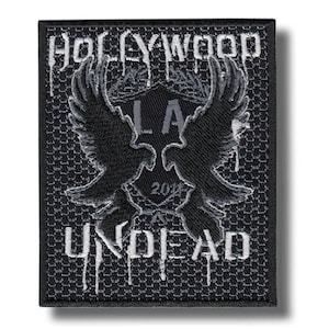May include: A rectangular black embroidered patch featuring the white text HOLLYWOOD at the top and UNDEAD at the bottom. In the center, a black eagle silhouette is displayed over a shield shape with the letters L.A. and the number 2011.