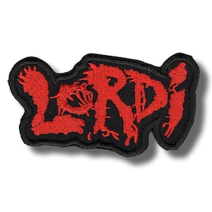 Op de afbeelding: Een geborduurde patch met het woord LORDI in een grillig, verweerd rood lettertype. De letters hebben een ruwe, getextureerde uitstraling met scherpe randen en zijn omlijnd door een dikke zwarte rand die de contouren van de tekst volgt.