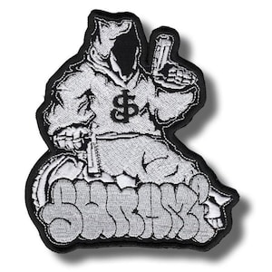 May include: An embroidered patch featuring a hooded figure in a light gray robe with a black dollar sign on the chest. The figure holds a handgun in one hand and a knife in the other. Below the figure, the word SURAZI is written in graffiti style.
