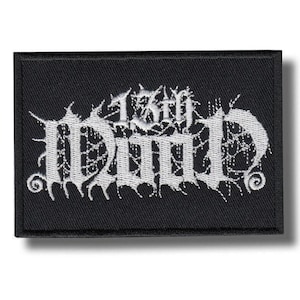May include: A rectangular black embroidered patch featuring white thread lettering that reads 13th MUD. The text is stylised with sharp, jagged edges and a web-like pattern integrated into the letters, all bordered by a thick black stitched edge.