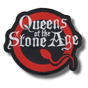 May include: A circular embroidered patch featuring a black background with a red ring border. The text Queens of the Stone Age is stitched in white lettering across the centre, accompanied by a red sperm-shaped icon at the bottom right.